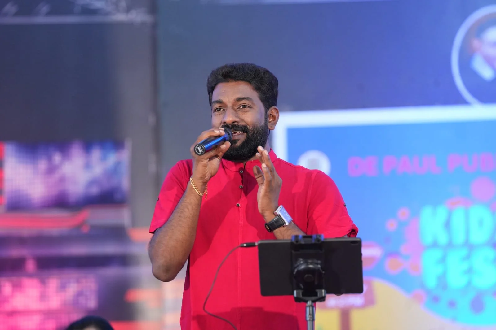 Arun Guinness singing into a microphone in a red shirt during a live stage show