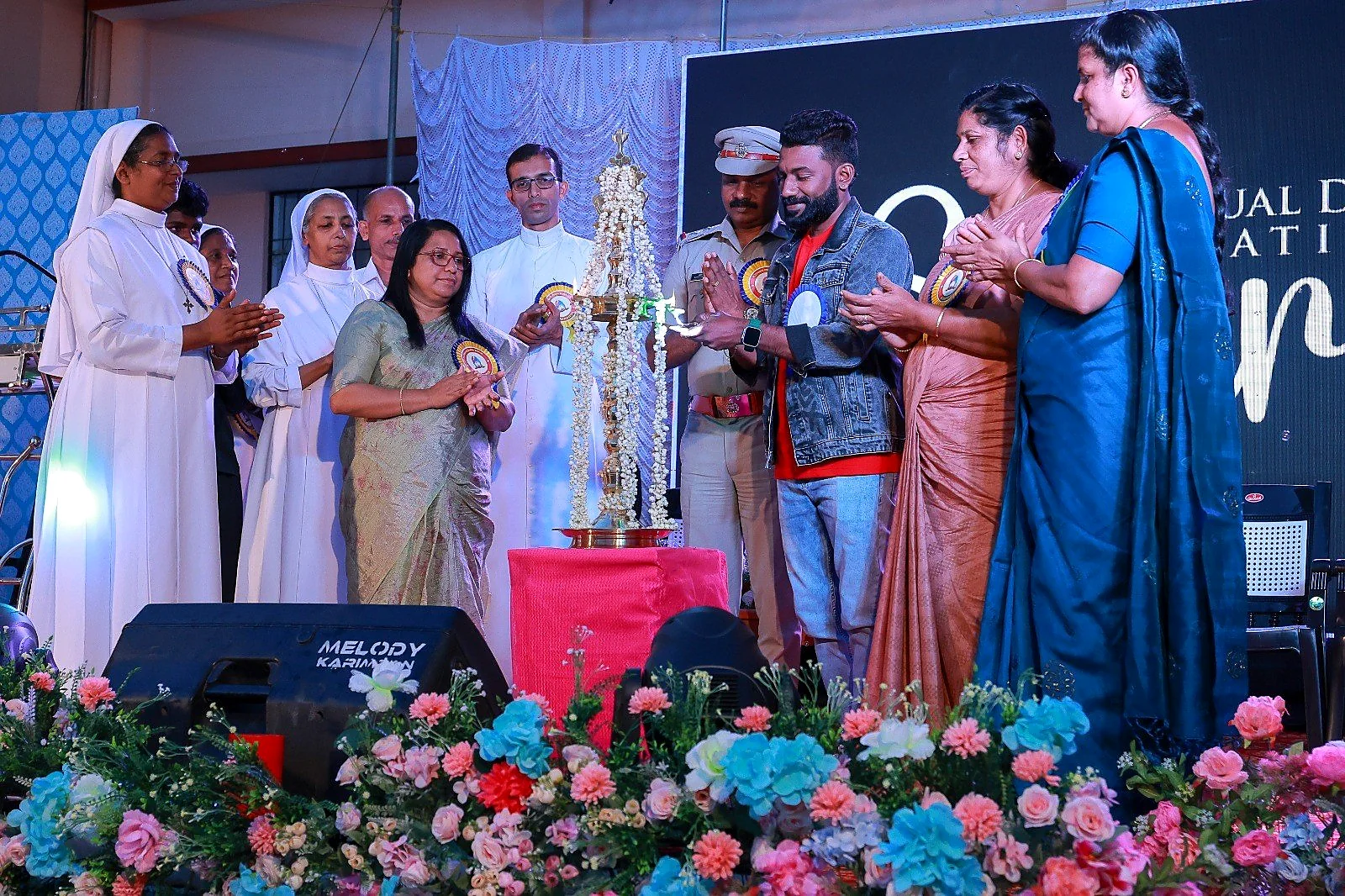 Arun Guinness joining guests for a ceremonial lamp lighting on a school stage
